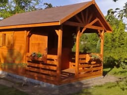 domek letniskowy z tarasem z bordowym dachem wśród drzew